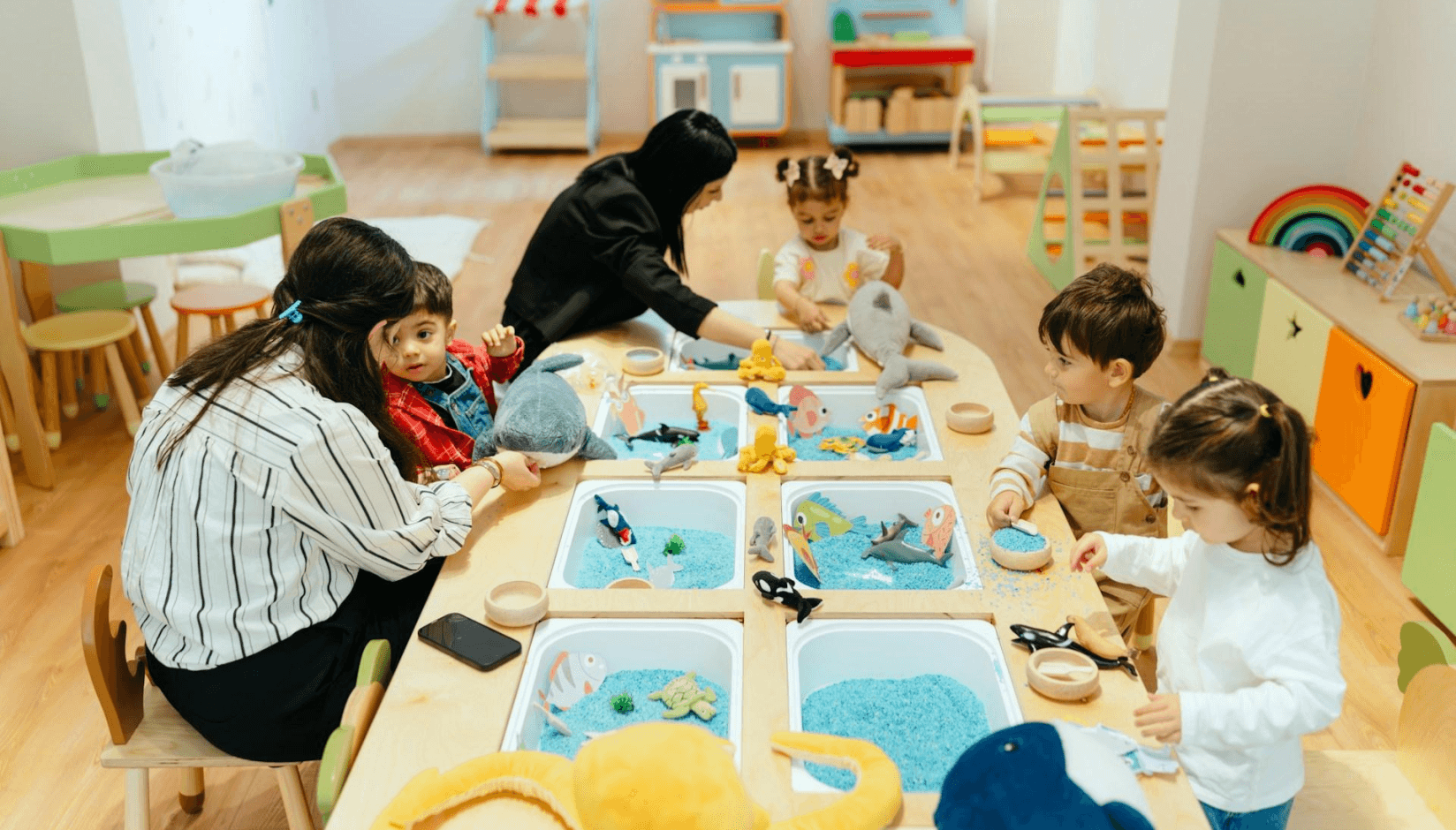 Childcare staff supervise young children in a bright on-site playroom inside a child-friendly coworking space, illustrating how coworking with childcare supports working parents through safe, professional family-friendly amenities.